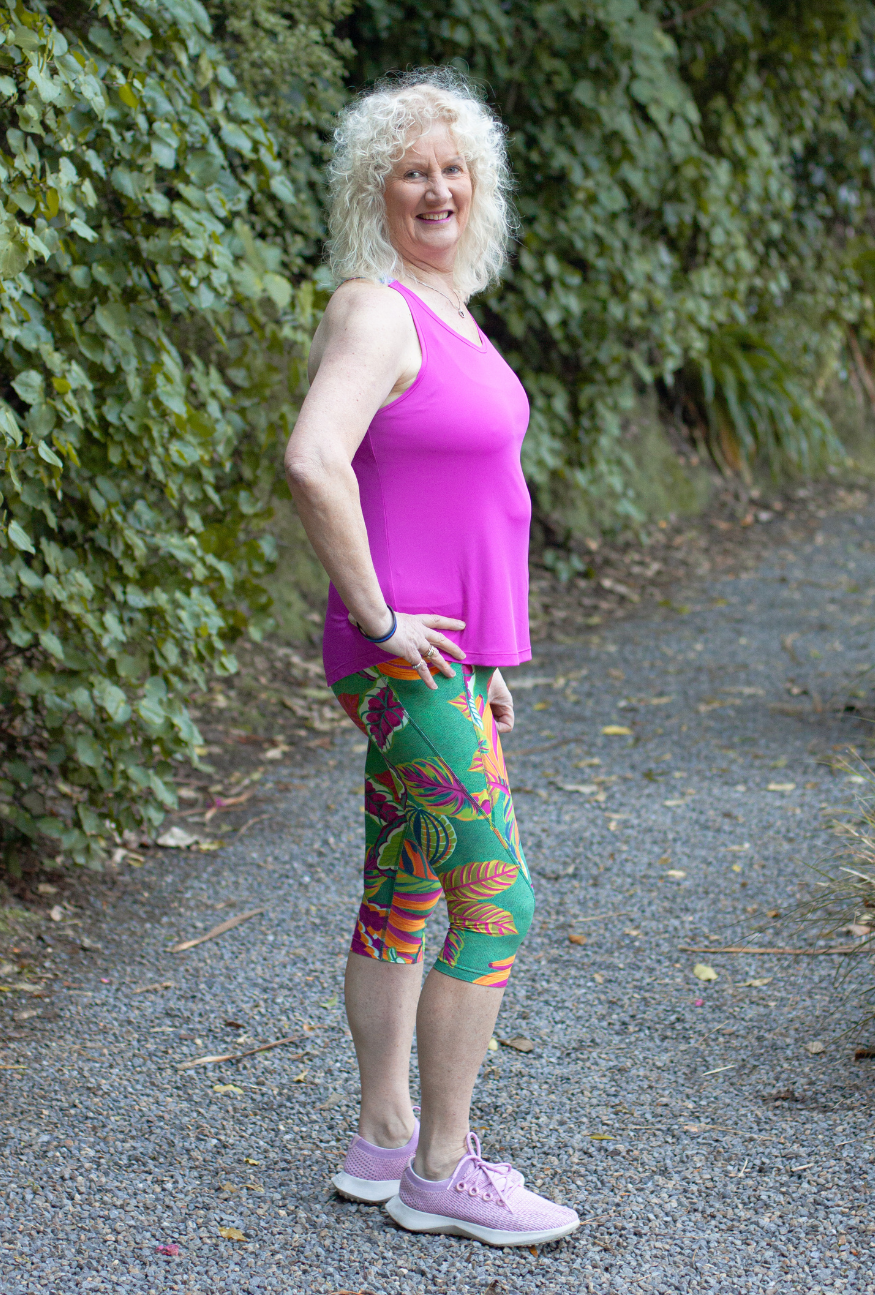 Woman in pink top and colourful Raumati print leggings standing on a gravel path with greenery in the background