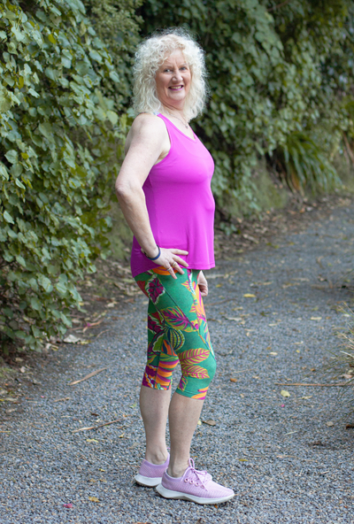Woman in pink top and colourful Raumati print leggings standing on a gravel path with greenery in the background