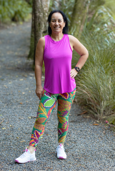 Woman in a bright pink sleeveless top and colourful leggings standing outdoors on a path.