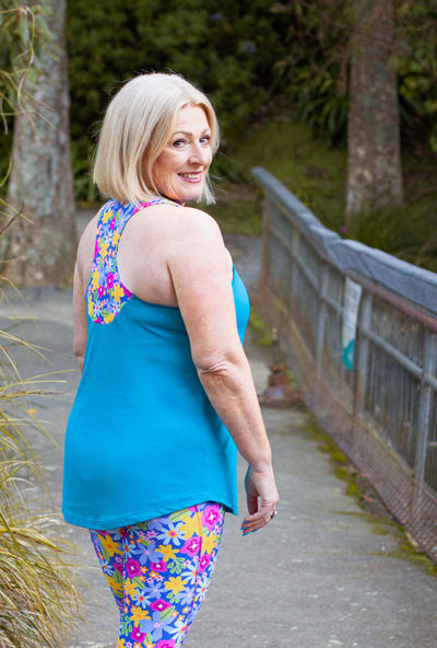 Woman wearing a blue tank top and colourful floral leggings walking outdoors.
