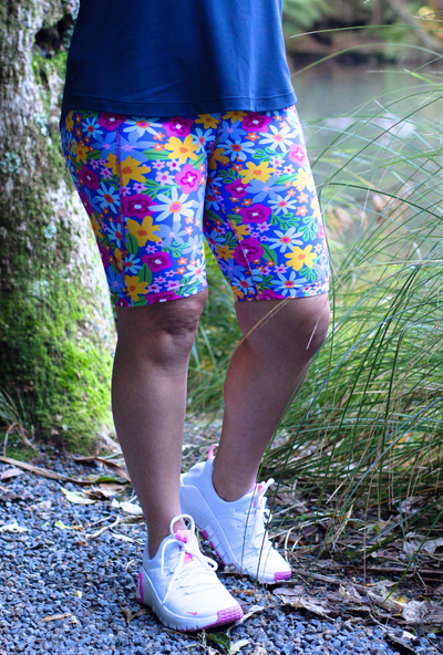 Person wearing colorful floral shorts and white sneakers in a natural setting.